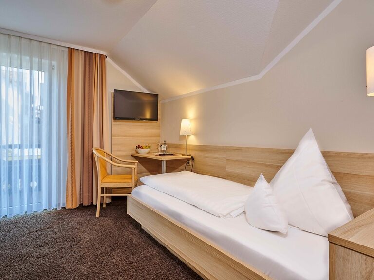 Das Einzelbett im ZimmerGänseblümchen an der Wand mit Fernseher.