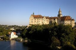 Das imposante Schloss Sigmaringen mit prächtiger Turmarchitektur liegt malerisch an einem Flussufer auf einem Hügel.
