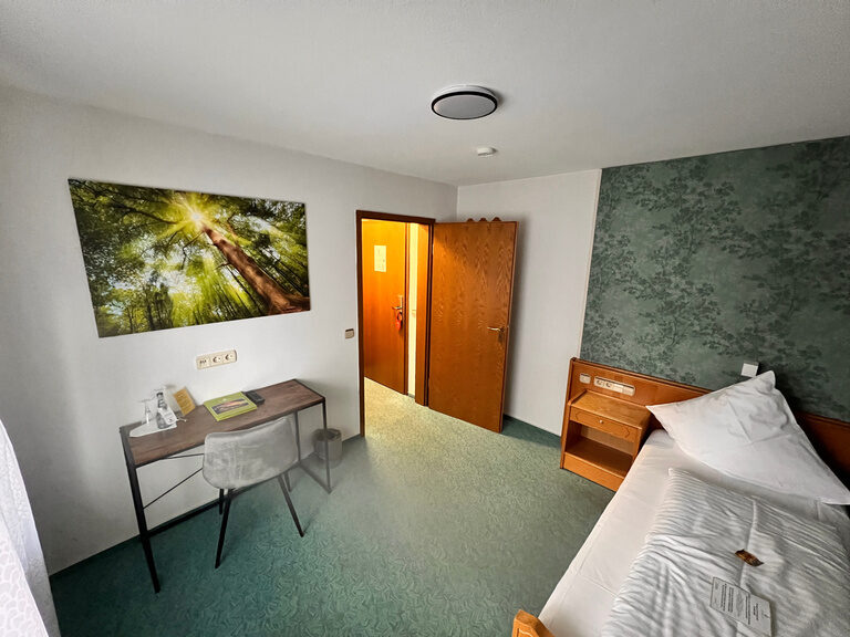 Ein komfortables Bett und ein Schreibtisch dominieren das ansprechend gestaltete Fuchsbau Hotelzimmer.